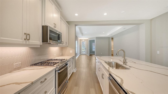 kitchen featuring a sink, backsplash, white cabinetry, stainless steel appliances, and light wood finished floors