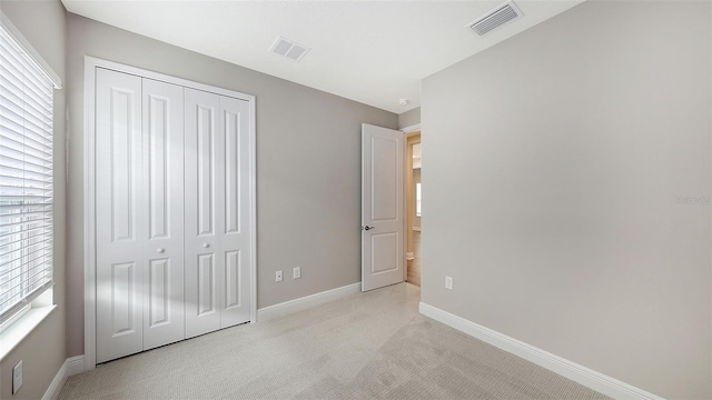 unfurnished bedroom featuring a closet, visible vents, light colored carpet, and baseboards