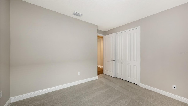 unfurnished bedroom featuring baseboards, visible vents, a closet, and light carpet