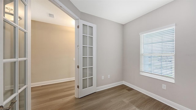 unfurnished room with visible vents, baseboards, wood finished floors, and french doors