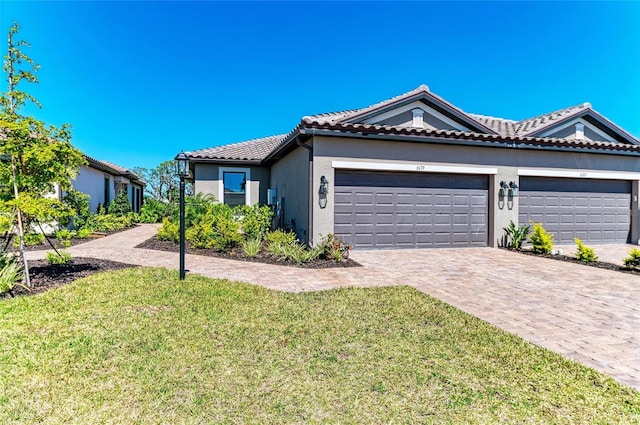 view of front of home with a front yard, stucco siding, a garage, a tile roof, and decorative driveway