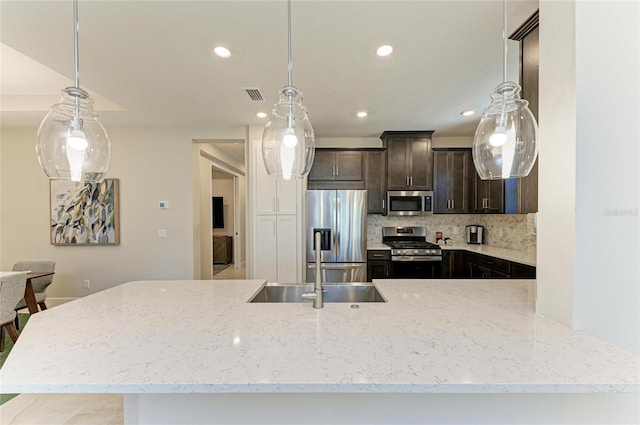 kitchen featuring tasteful backsplash, dark brown cabinets, appliances with stainless steel finishes, and light stone countertops