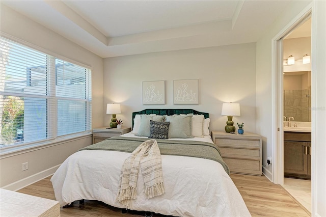 bedroom with a tray ceiling, baseboards, light wood-type flooring, and a sink