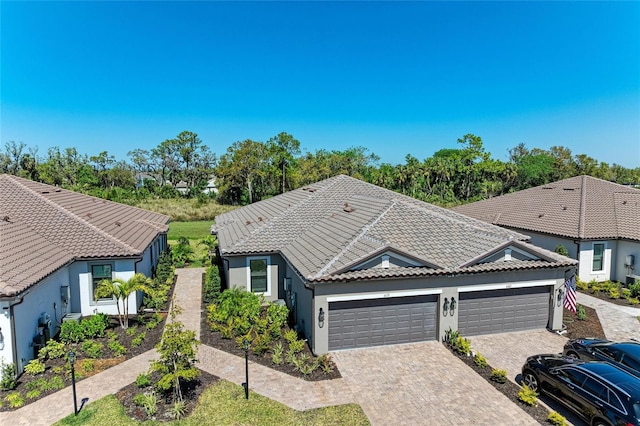 ranch-style house featuring a tile roof, decorative driveway, a garage, and stucco siding