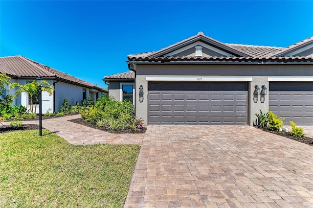 view of front of house with stucco siding, decorative driveway, a front yard, a garage, and a tiled roof