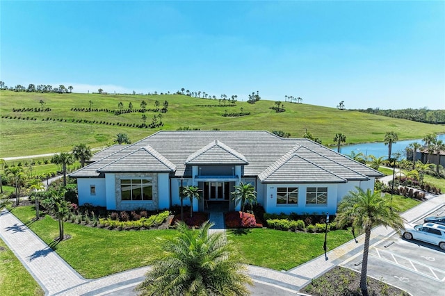 view of front facade with stucco siding, a tile roof, a front yard, and a water view