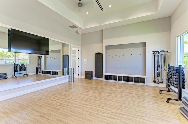 workout room featuring visible vents, baseboards, a high ceiling, wood finished floors, and a raised ceiling