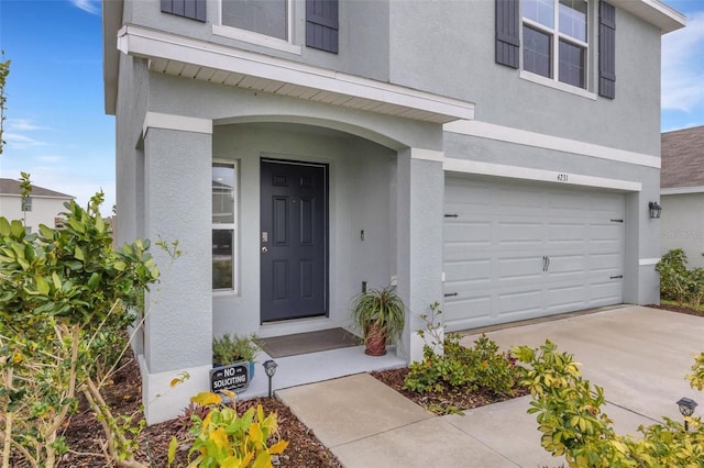 doorway to property featuring stucco siding, an attached garage, and driveway