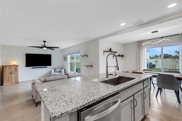 kitchen featuring light stone countertops, an island with sink, light tile patterned floors, stainless steel dishwasher, and a sink