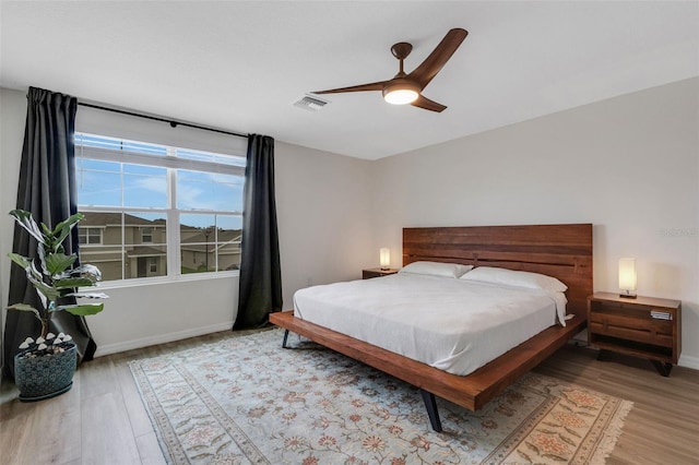 bedroom featuring visible vents, a ceiling fan, baseboards, and wood finished floors