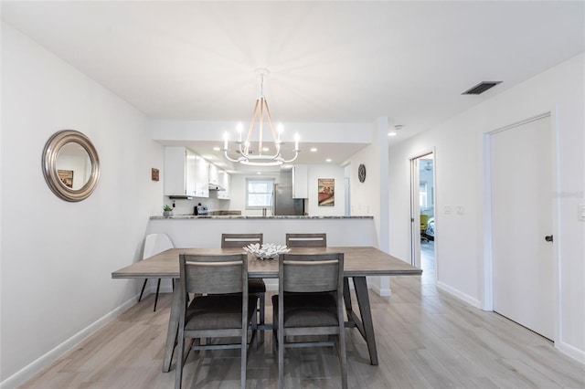 dining space with baseboards, light wood-style floors, visible vents, and a chandelier