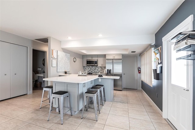 kitchen with gray cabinets, backsplash, stainless steel appliances, a breakfast bar area, and light countertops