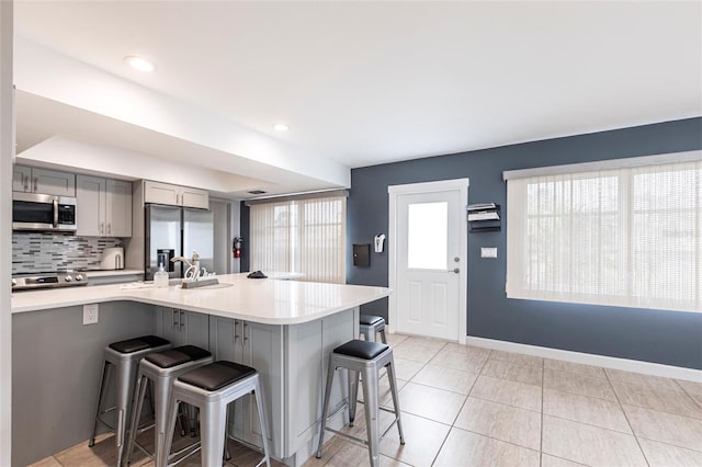 kitchen with tasteful backsplash, gray cabinetry, a breakfast bar, light countertops, and stainless steel appliances