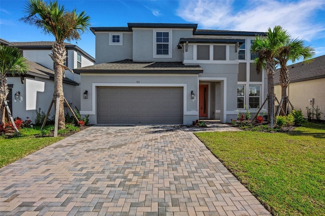 prairie-style home with stucco siding, decorative driveway, and a front yard