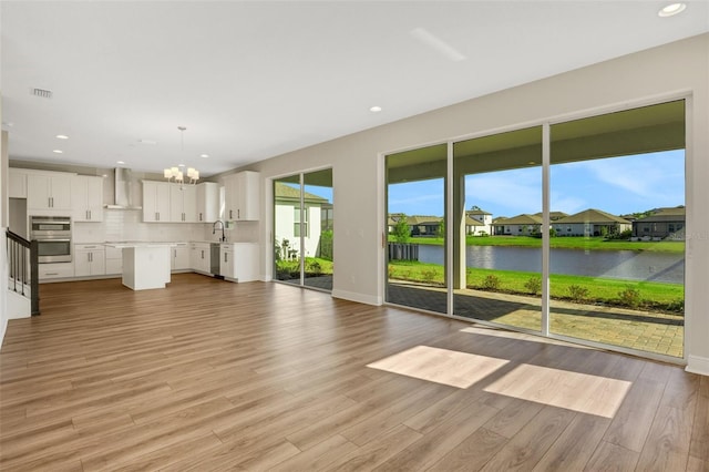 unfurnished living room featuring visible vents, a water view, a sink, light wood-style floors, and an inviting chandelier