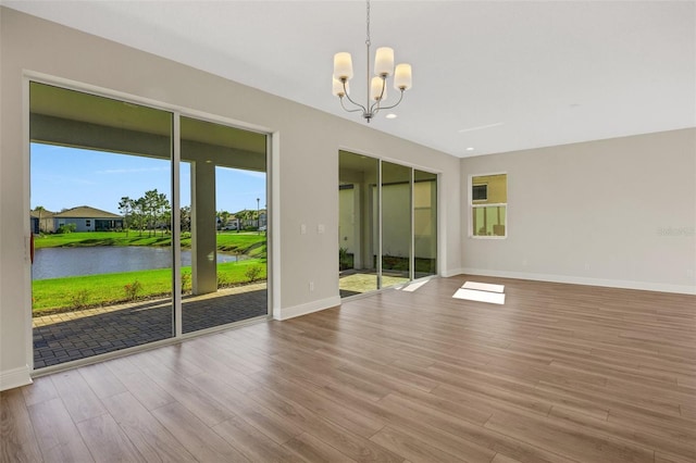 empty room featuring wood finished floors, baseboards, recessed lighting, a water view, and a chandelier