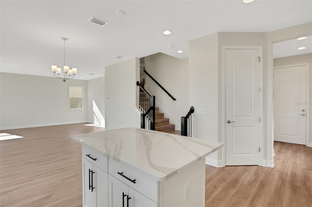 kitchen with hanging light fixtures, light stone counters, white cabinetry, and light wood finished floors