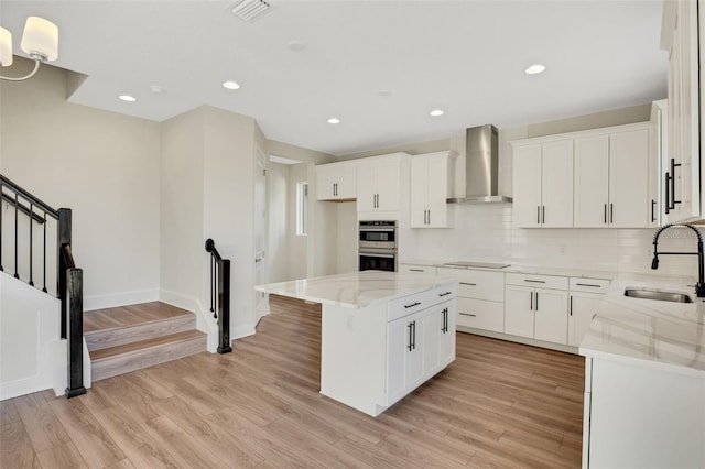 kitchen featuring visible vents, wall chimney range hood, light stone countertops, black electric cooktop, and a sink