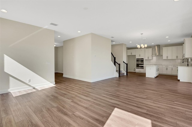 unfurnished living room featuring visible vents, light wood-style flooring, a sink, an inviting chandelier, and stairs