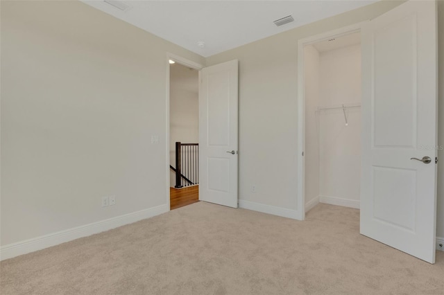 unfurnished bedroom with a spacious closet, visible vents, light colored carpet, and baseboards