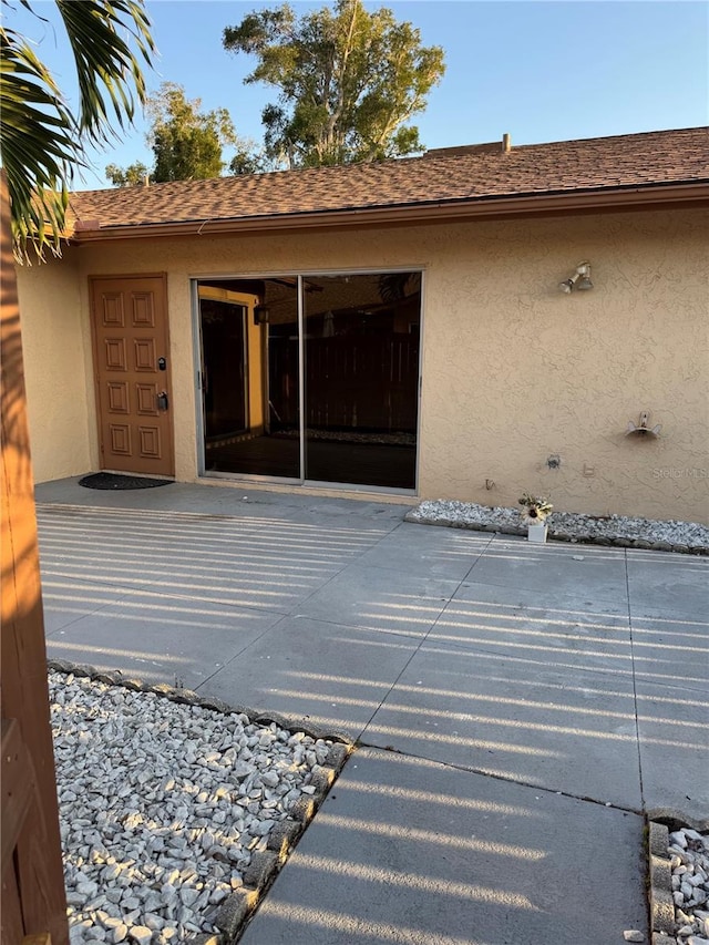 exterior space featuring stucco siding, a patio, and roof with shingles