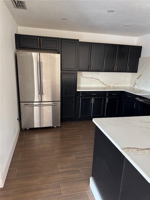 kitchen with dark cabinets, visible vents, freestanding refrigerator, and wood tiled floor