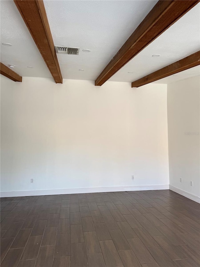 spare room with visible vents, beamed ceiling, baseboards, and dark wood-style flooring