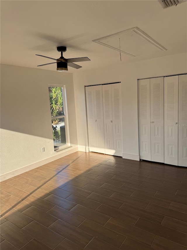 unfurnished bedroom featuring wood finish floors, two closets, attic access, and ceiling fan