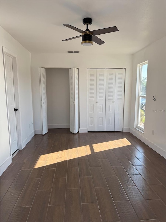 unfurnished bedroom with visible vents, wood finish floors, baseboards, multiple closets, and a ceiling fan