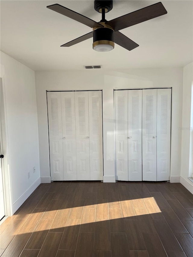 unfurnished bedroom with a ceiling fan, baseboards, visible vents, wood tiled floor, and two closets