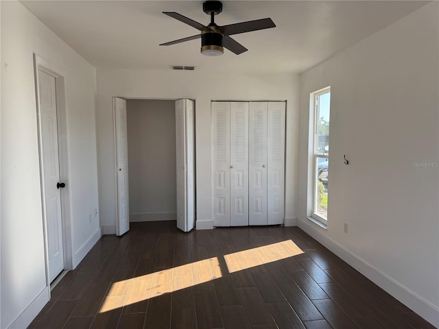 unfurnished bedroom with dark wood-style floors, visible vents, multiple windows, and multiple closets