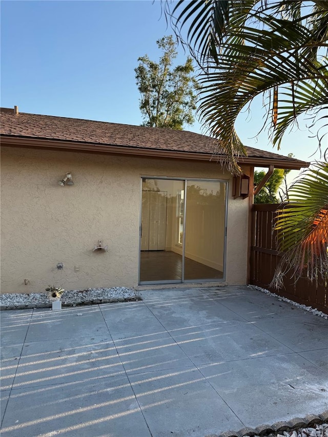 rear view of house with stucco siding, roof with shingles, and a patio area