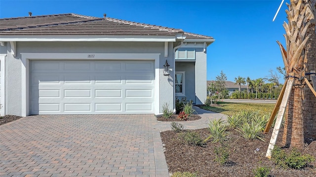 view of front of house with a tiled roof, decorative driveway, an attached garage, and stucco siding