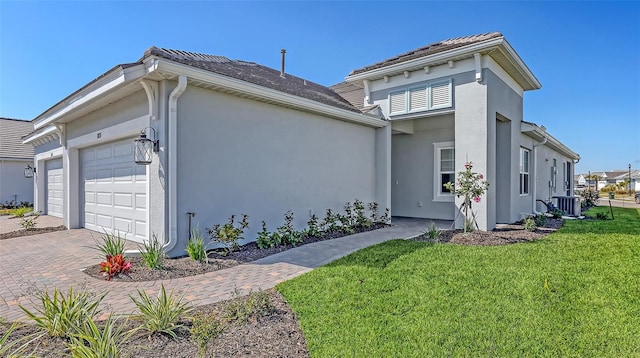 view of front of home featuring a front yard, central AC, stucco siding, decorative driveway, and an attached garage