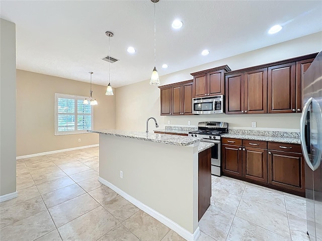 kitchen featuring light stone counters, stainless steel appliances, pendant lighting, and a kitchen island with sink