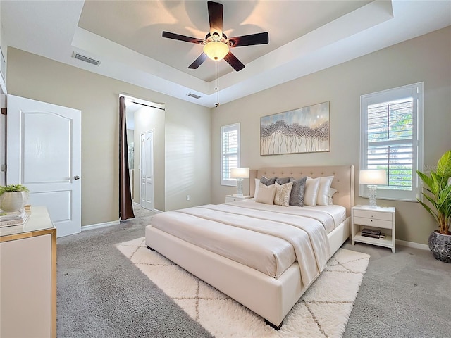 carpeted bedroom with visible vents, baseboards, a tray ceiling, and a ceiling fan