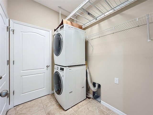 clothes washing area featuring light tile patterned floors, laundry area, stacked washing maching and dryer, and baseboards