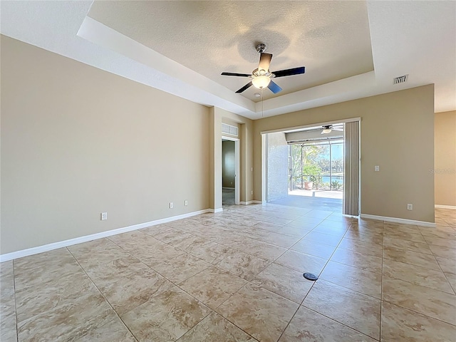 spare room with visible vents, baseboards, ceiling fan, a tray ceiling, and a textured ceiling