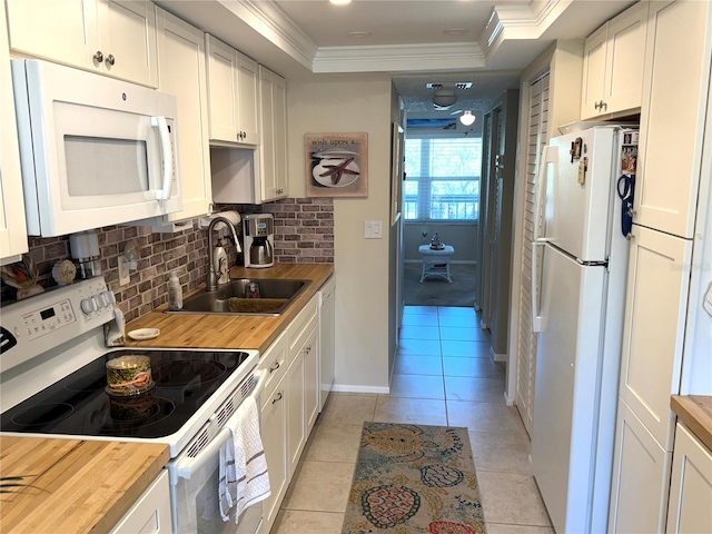 kitchen with ornamental molding, a raised ceiling, white appliances, wood counters, and a sink