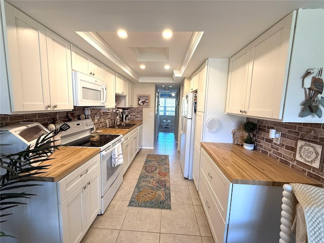 kitchen with white appliances, a tray ceiling, a sink, tasteful backsplash, and butcher block counters