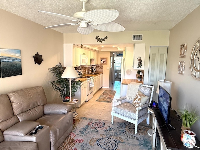 living area with light tile patterned floors, a ceiling fan, visible vents, and a textured ceiling