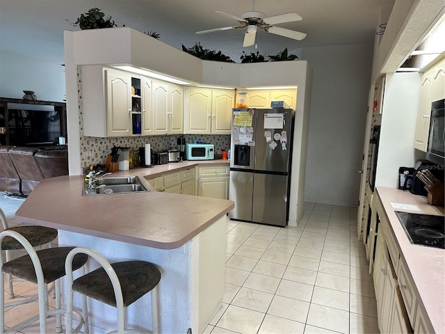 kitchen featuring tasteful backsplash, a breakfast bar, a peninsula, black appliances, and a sink