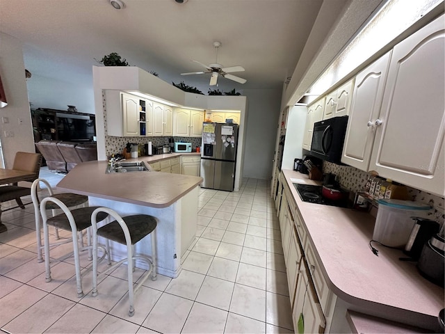 kitchen with a breakfast bar area, a peninsula, a sink, decorative backsplash, and black appliances