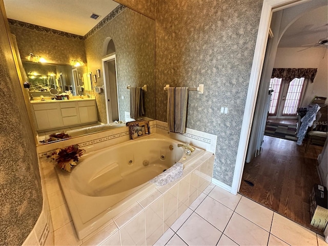 full bath featuring a jetted tub, wallpapered walls, tile patterned floors, vanity, and a ceiling fan