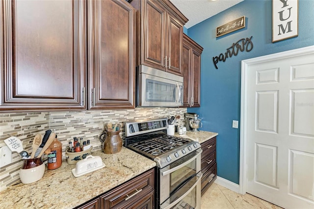 kitchen with backsplash, light stone counters, stainless steel appliances, light tile patterned flooring, and a textured ceiling