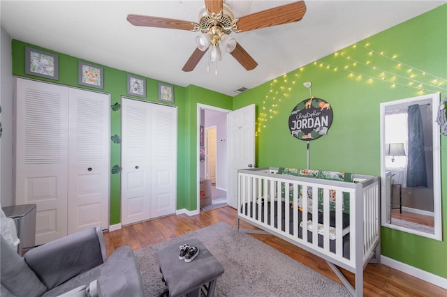 bedroom with visible vents, baseboards, multiple closets, wood finished floors, and a nursery area