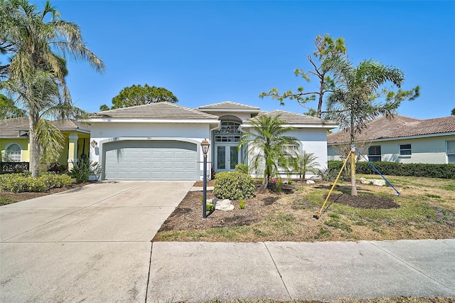 view of front of house with stucco siding, concrete driveway, french doors, a garage, and a tiled roof