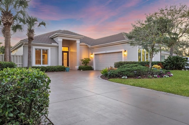 view of front of house featuring a tile roof, a front yard, stucco siding, driveway, and an attached garage