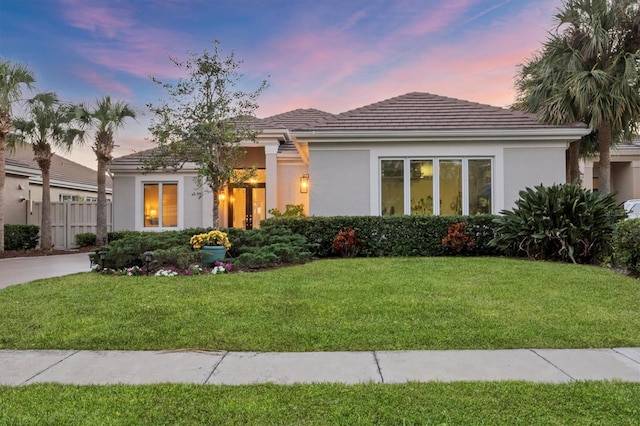 view of front of home with stucco siding, a lawn, and fence