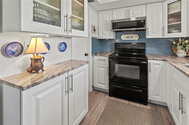 kitchen with light wood-type flooring, stainless steel microwave, tasteful backsplash, black / electric stove, and white cabinets